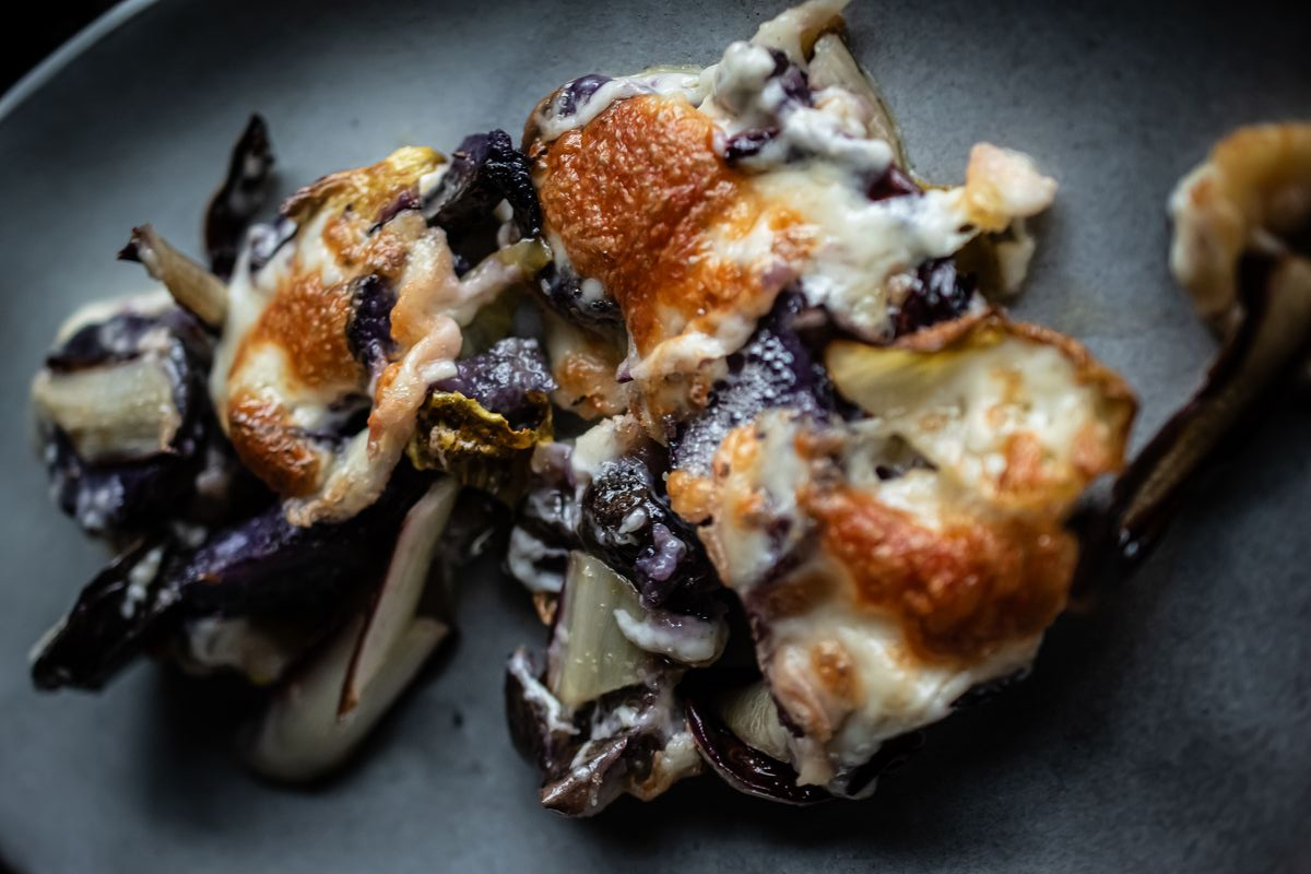 Nahaufnahme von violetten Kartoffelscheiben mit geschmolzenem Taleggio auf dunklem Teller von Gewürzmühle Rosenheim