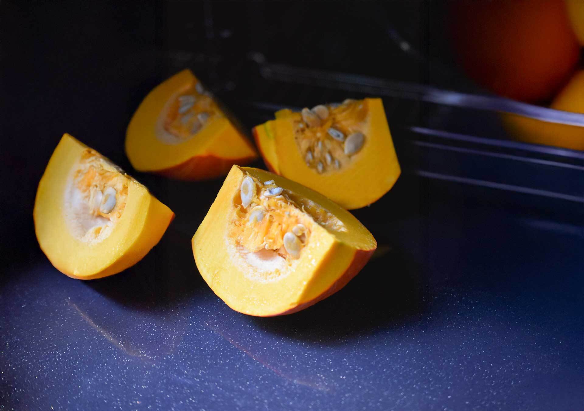 Mehrere Stücke eines frischen Hokkaido-Kürbisses liegen auf einer dunklen Arbeitsfläche. Die orangene Farbe und die Kürbiskerne sind deutlich erkennbar – Herbstgemüse im Rohzustand, fotografiert für die Gewürzmühle Rosenheim.