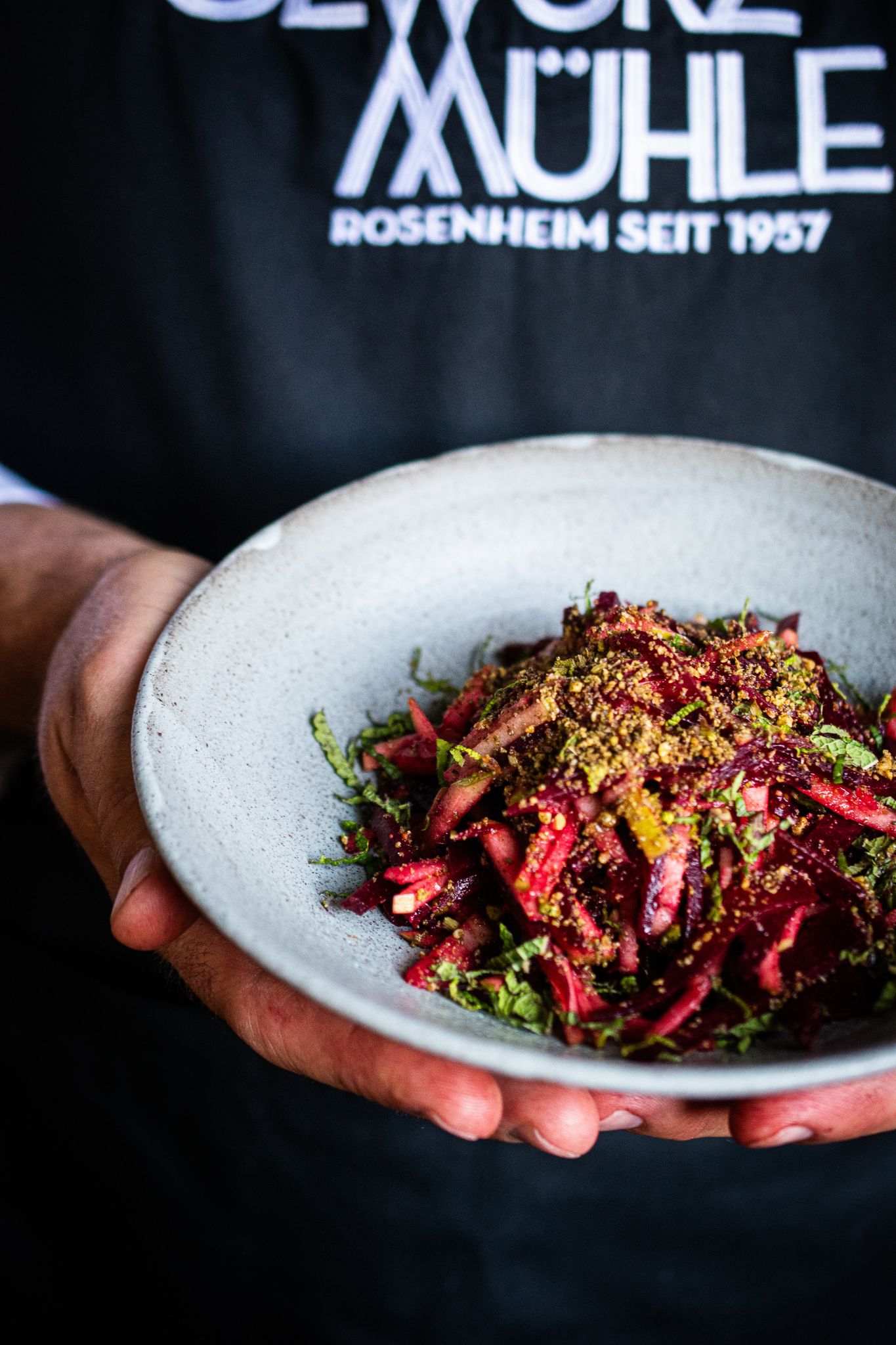 Teller mit Salat aus Rote Bete und Apfel - getoppt mit Dukkah Gewürzmischung in den Händen eines Menschen gehalten