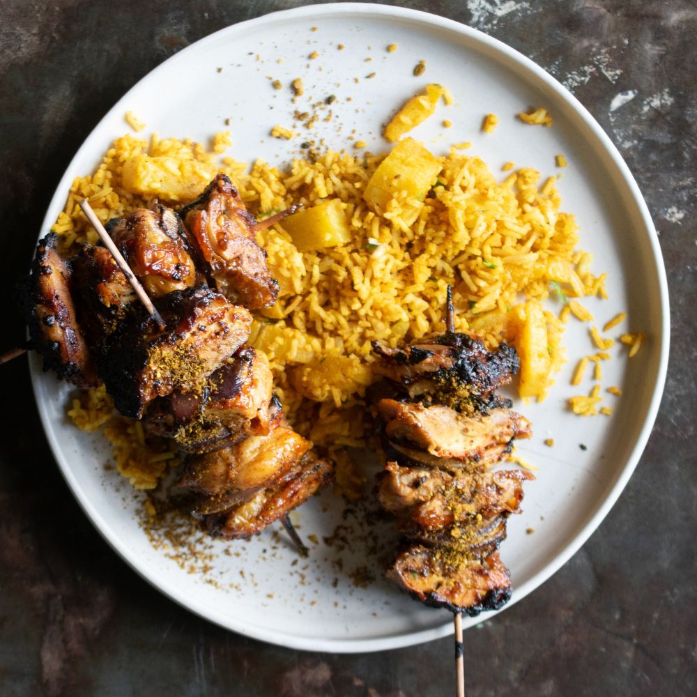 Gegrillte Hähnchenspieße mit gelbem Curryreis und Ananasstücken auf einem großen hellen Teller.