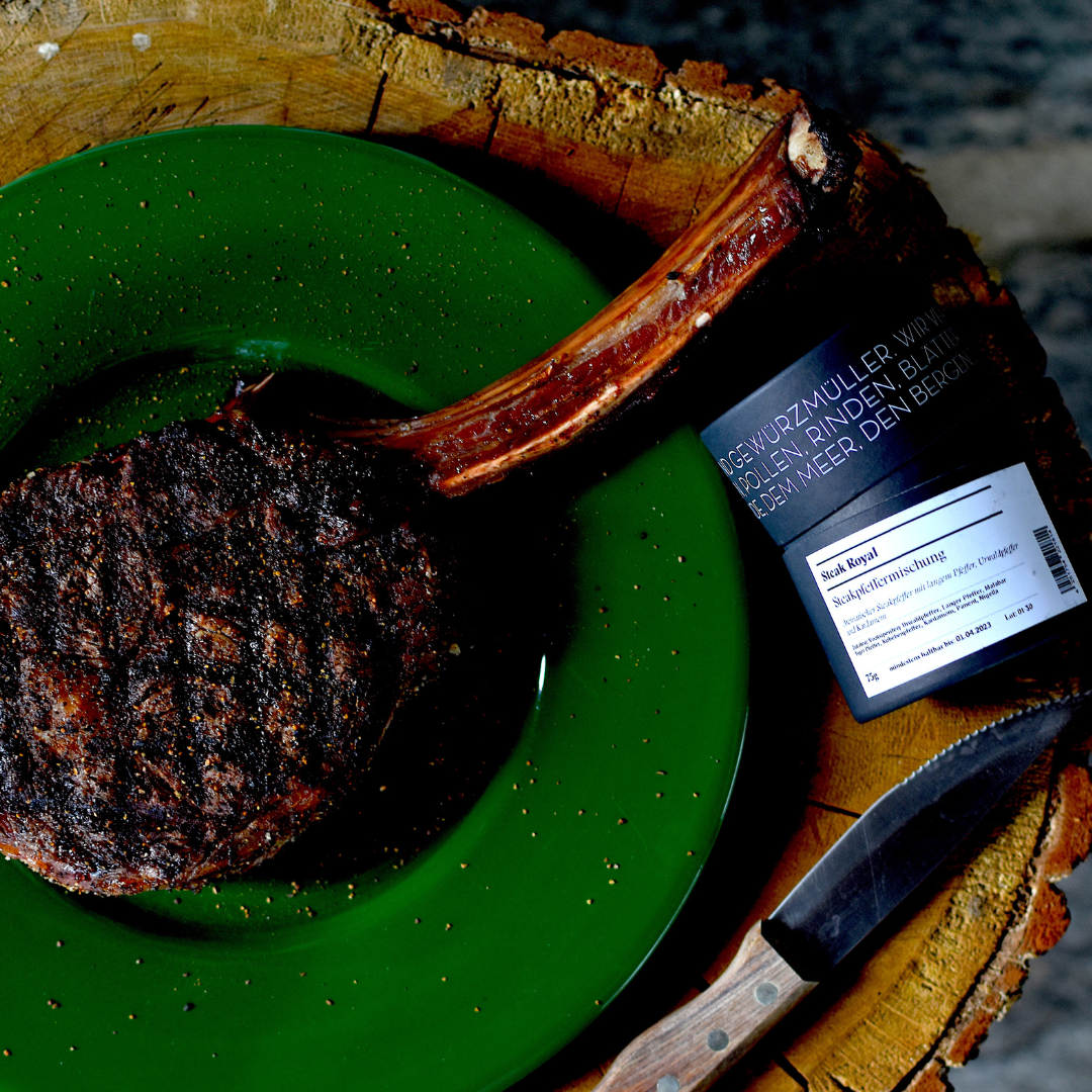 Gegrilltes Steak auf grünem Teller mit Steakgewürz und Messer, angerichtet auf einem Holzbrett