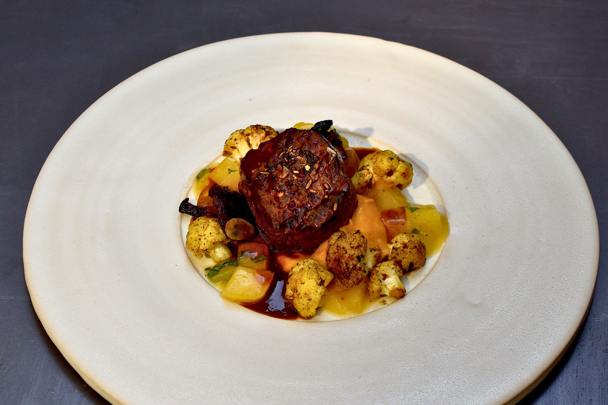 Rinderfilet mit Suesskartoffelcreme und Chutney angerichtet auf einem weißen Teller.