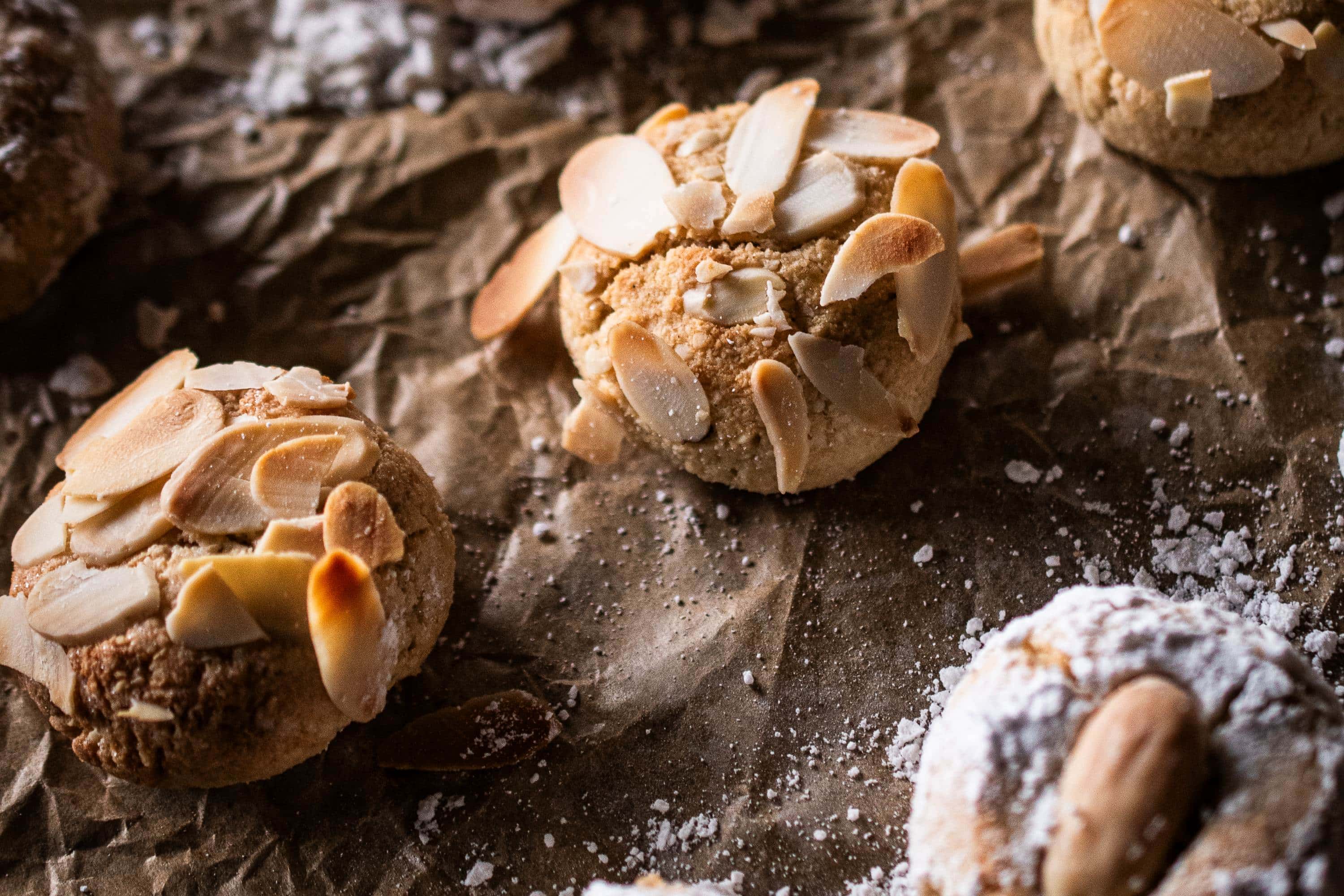 Frisch gebackene Amaretti Morbidi mit Mandelblättchen auf braunem Backpapier, locker mit Puderzucker bestreut
