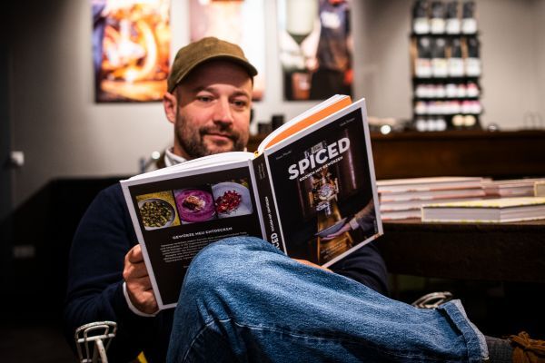 Simon Mendel sitzt in einem Stuhl und ließt im "SPICED" Kochbuch