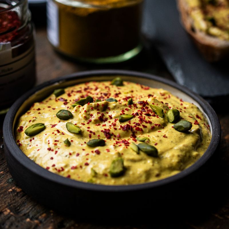 Orient-Curry-Creme und Pul Biber (Aleppo Chili) in einer schwarzen Schale. Im Hintergrund Gläser der Gewürzmühle Rosenheim mit Curry- und Chilimischungen.