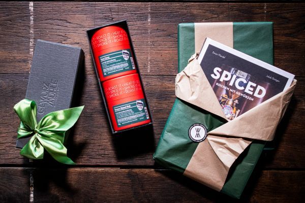 Das "SPICED" Kochbuch verpackt in Geschenkpapier und eine Geschenkpaket aus der Gewürzmühle daneben liegend mit zwei Gewürzen darin