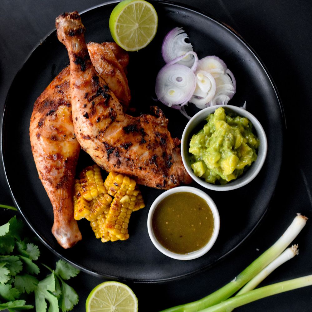 Jamaican Jerk Rub Ein Teller mit zwei Hühnerschenkel mit Jamaican Jerk Chicken glasiert, serviert mit etwas Mais Guacamole und einem Dip.