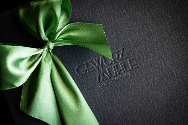 Nahaufnahme einer hochwertigen schwarzen Geschenkbox der Gewürzmühle Rosenheim mit geprägtem Logo und einer großen, glänzenden grünen Satinschleife.