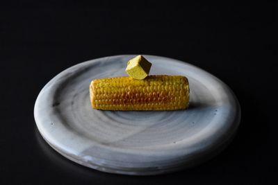 Maiskolben mit Gewürzbutterwürfel serviert, schwarzer Untergrund