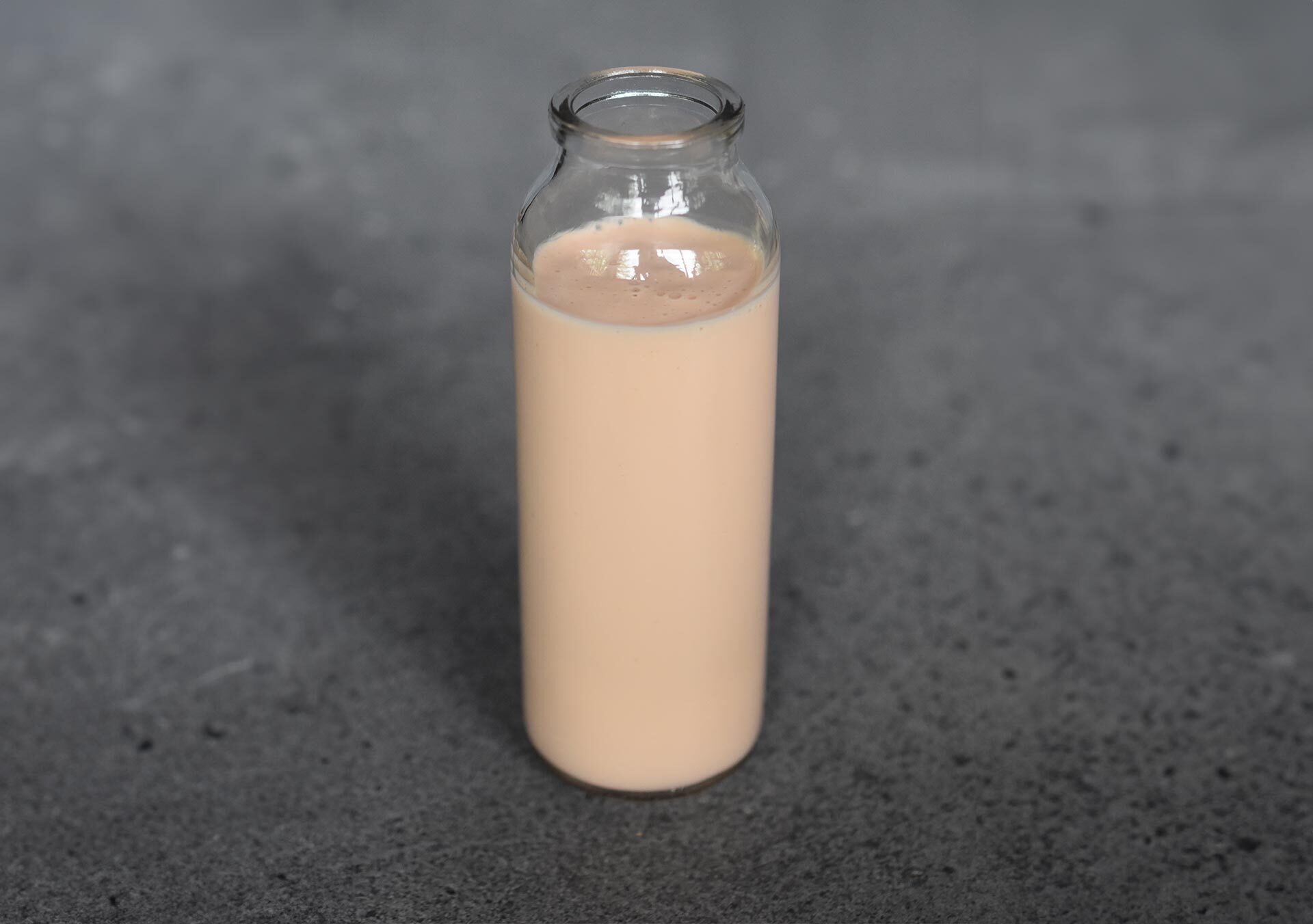 Glasflasche mit selbstgemachtem Grapefruit-Cassis-Dressing auf dunklem Untergrund