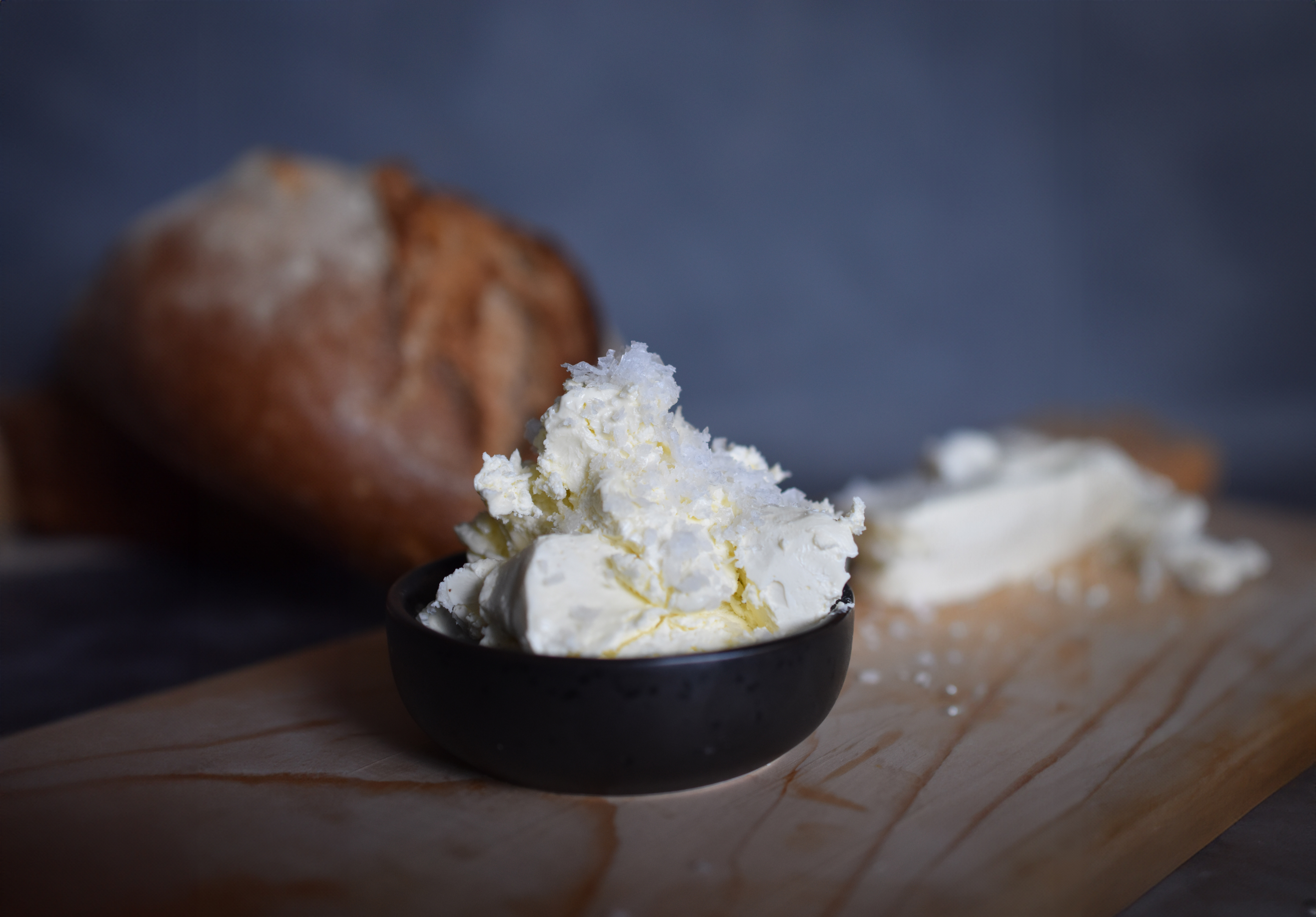 Olivenöl-Butter mit Snufnugg-Schneeflockesalz in schwarzer Schale auf einem Holzbrett