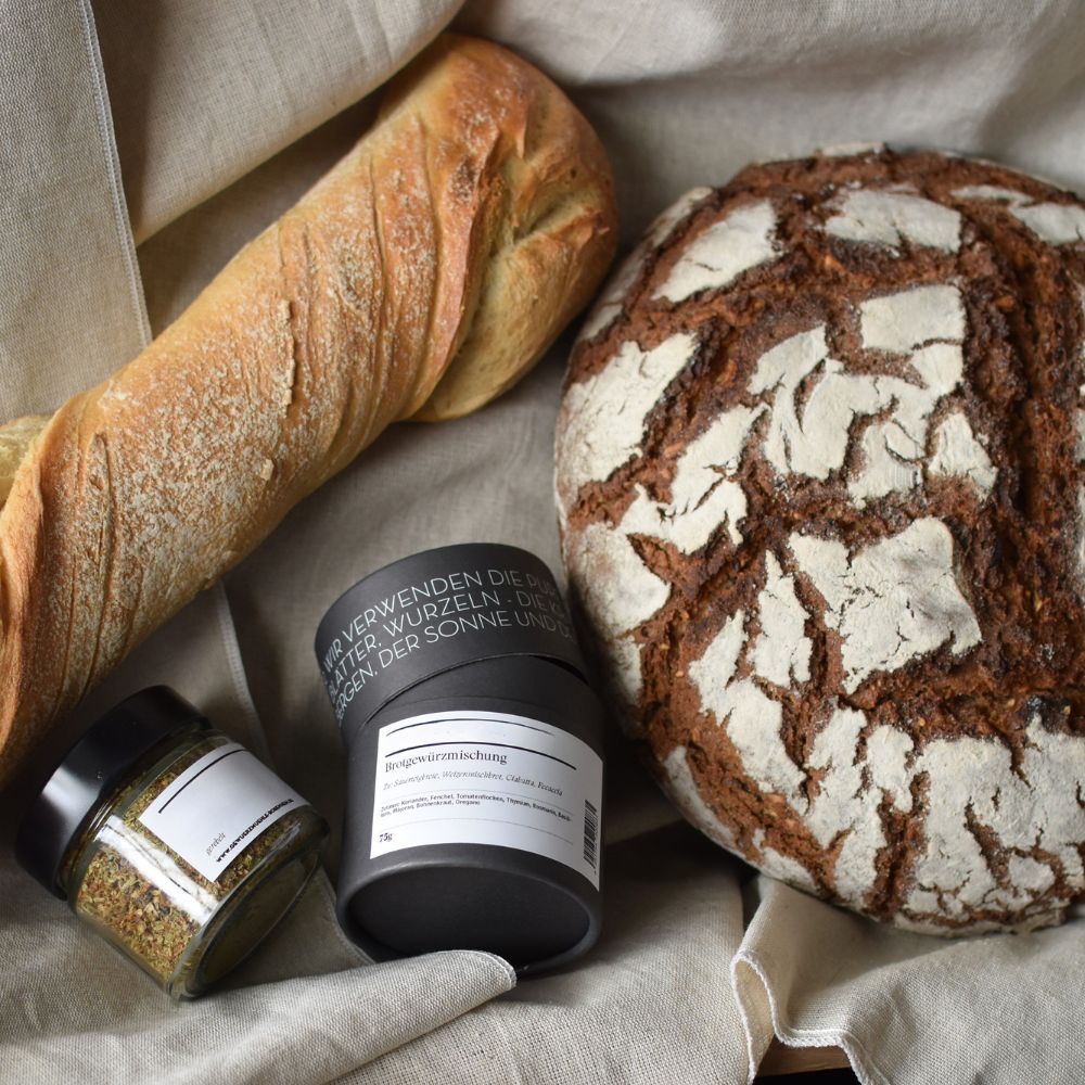 Brotgewürz, Würzlaib, geschrotet Brot und Baguette mit Gewürzdose daneben