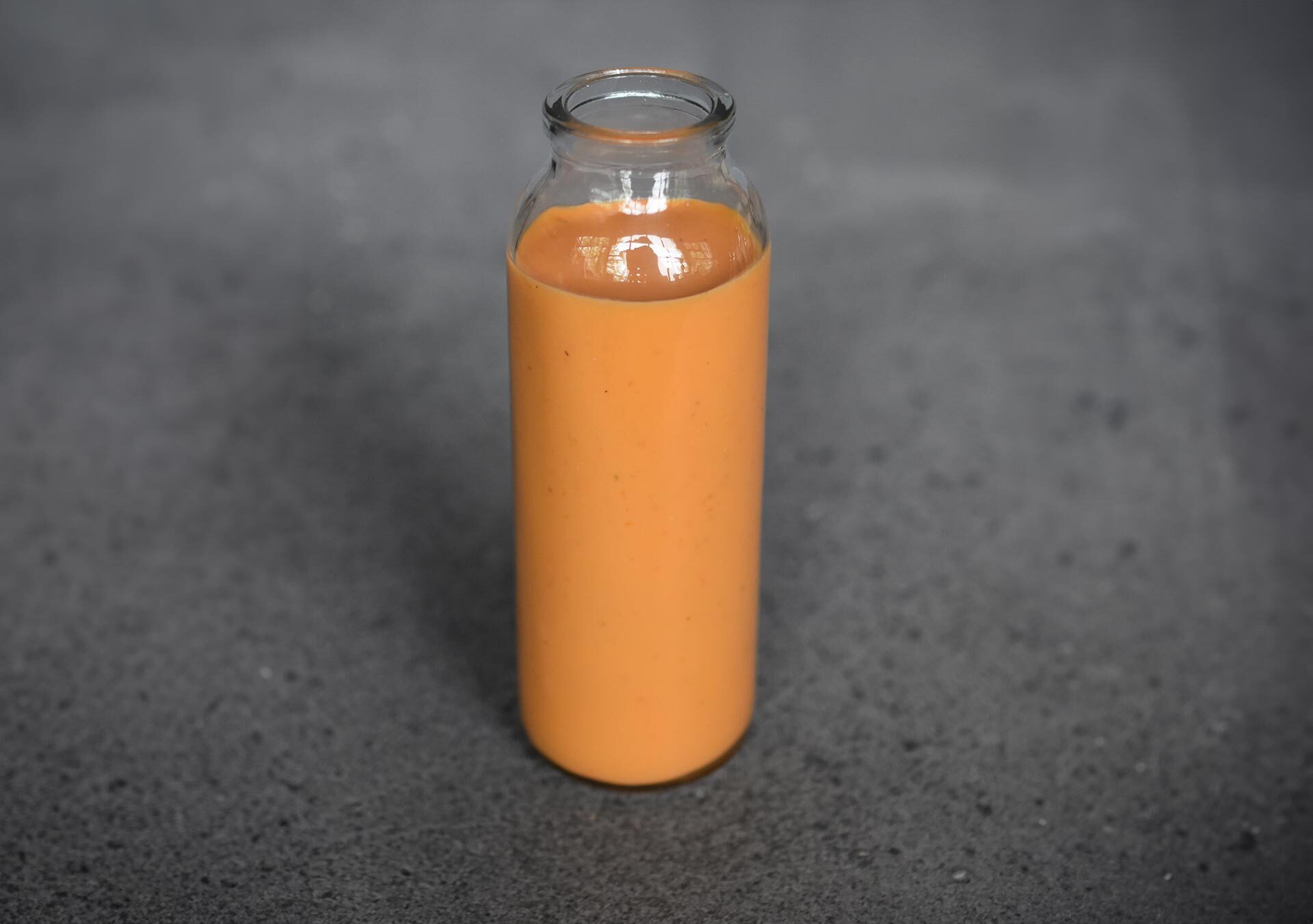 Glasflasche mit selbstgemachtem Tomaten-Dressing auf dunklem Untergrund