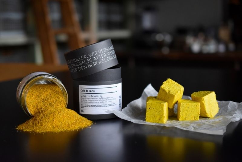 Zwei Cafe de Paris Gewürzdosen und gewürzte Butterwürfel auf einem Tisch stehend