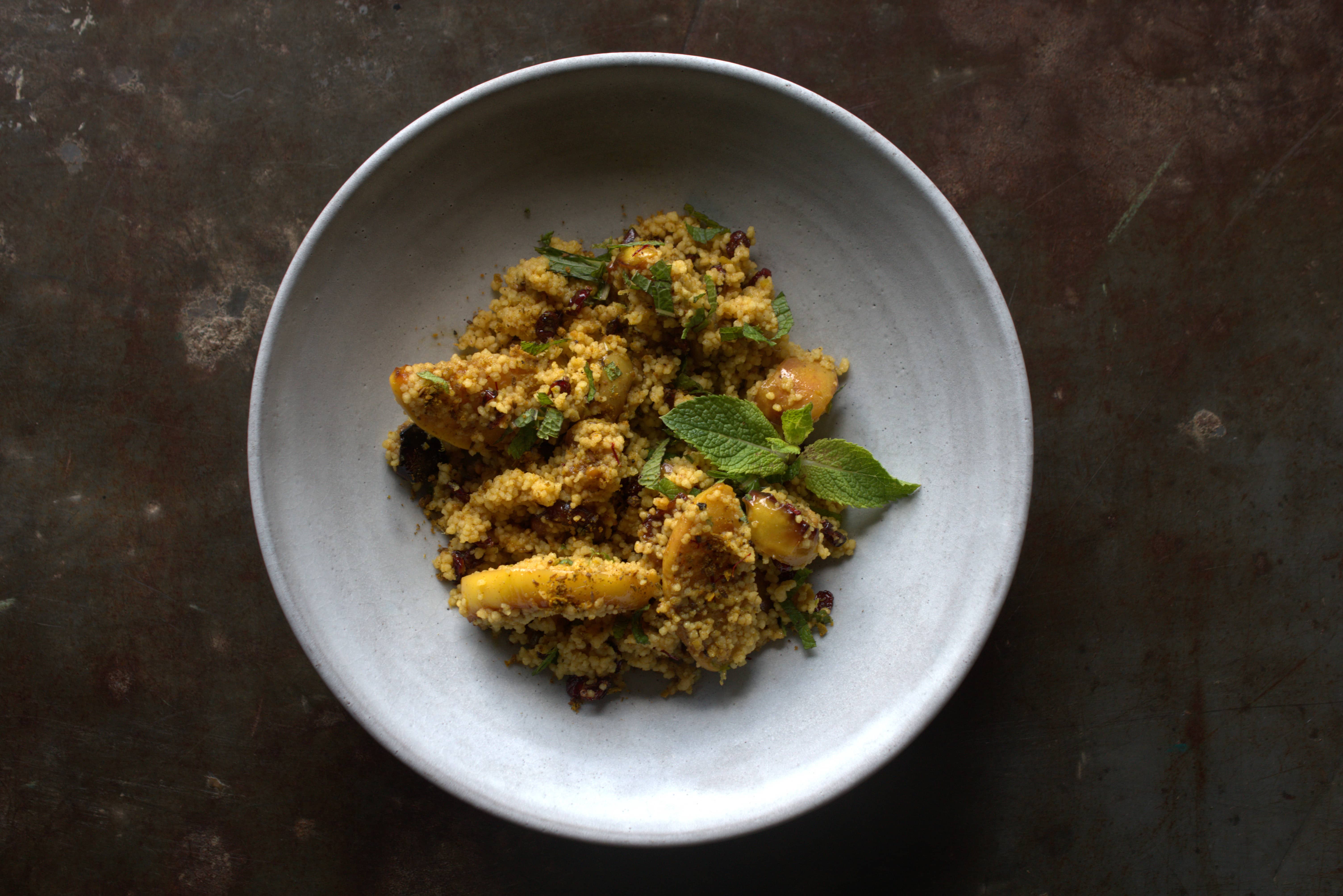 Orangen-Couscous mit geröstetem Apfel, Berberitzen, Vadouvan und frischer Minze, angerichtet in einer hellen Schale.