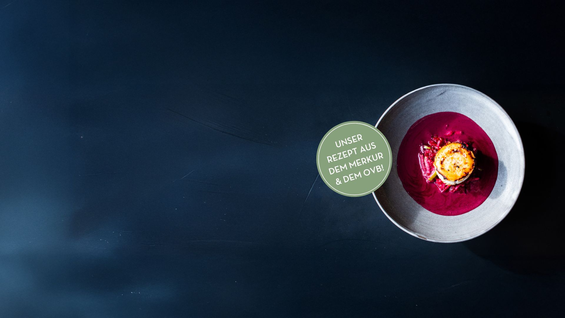 Rechts steht ein Teller auf dunklem Untergrund. Im Teller befindet sich gratinierter Ziegenkäse mit Rote Beete und Purple Curry.