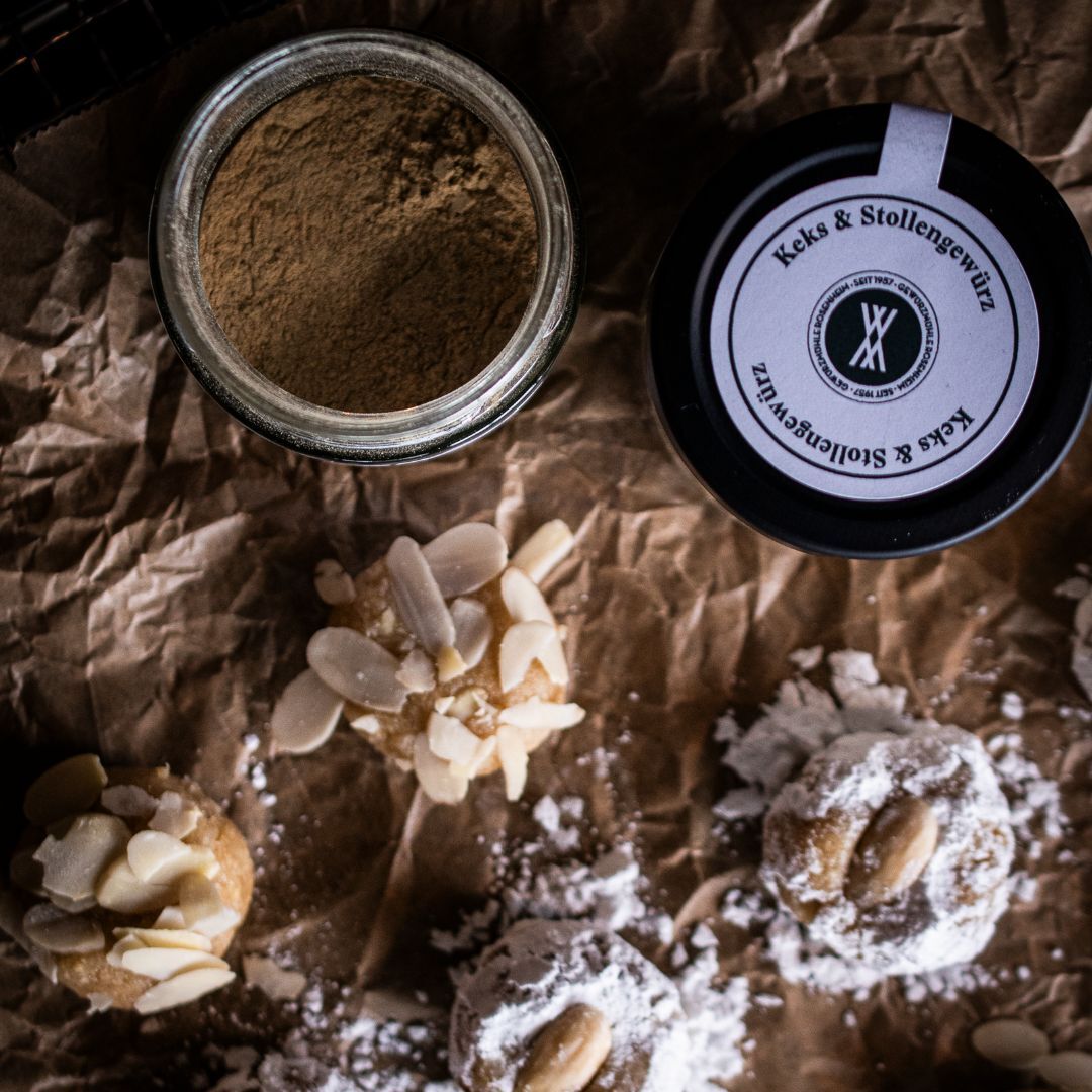 Vier Amaretti Morbidi liegen auf Backpapier und ein geöffnetes Gewürzglas mit Keks- & Stollengewürz steht daneben.