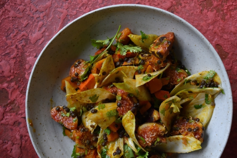 Kürbis-Linsen-Salat, gewürzt mit Ras El Hanout, serviert auf Teller auf rotem Untergrund
