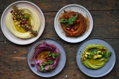 Vier Teller mit Hummus-Gerichte, von oben fotografiert.