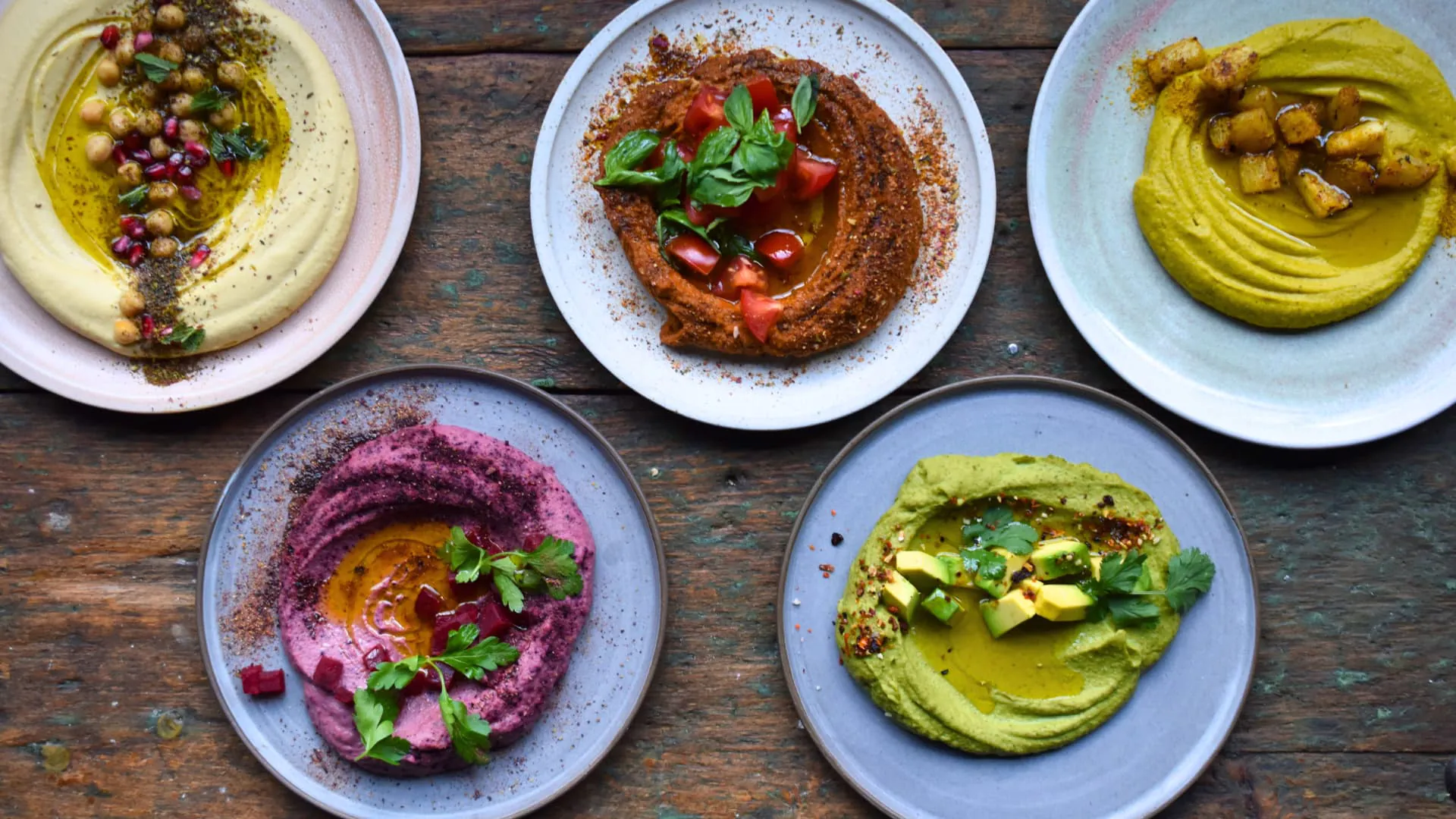 Fünf Teller mit Hummus-Gerichte, von oben fotografiert.