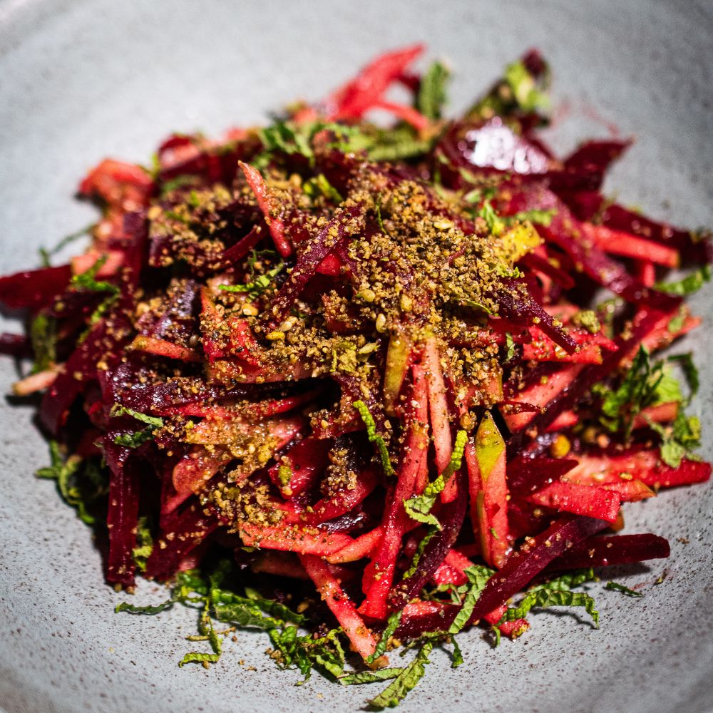 Dukkah (Ducca) Grauer Teller mit einer Portion Apfel-Rote-Bete-Salat mit etwas Dukkah-Gewürzmischung auf dem Salat und fein geschnittener Minze