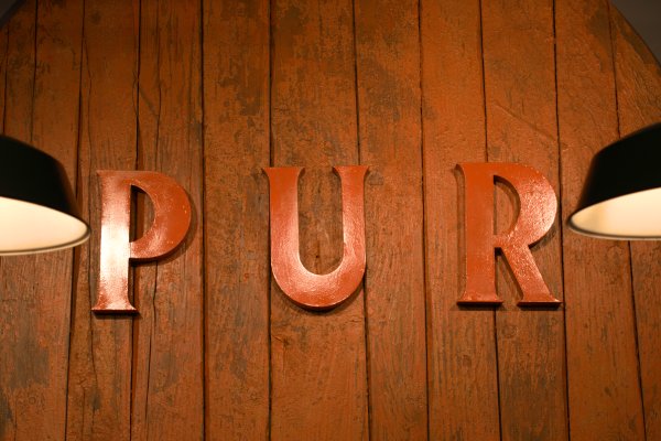 Detailaufnahme der rustikalen Innenraumgestaltung im Gewürzladen der Gewürzmühle Rosenheim in Nürnberg mit großen roten Buchstaben „PUR“ an einer Holzwand und stimmungsvoller Beleuchtung.