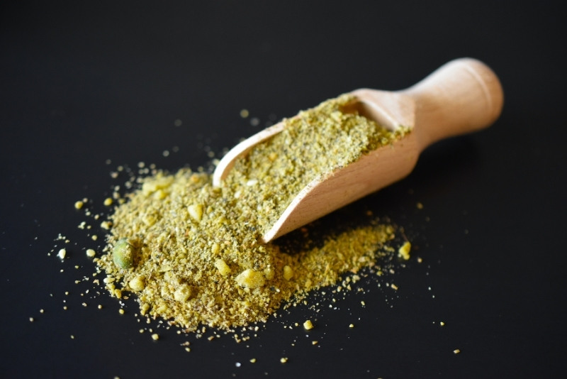 Dukkah in einer Holzschaufel auf schwarzem Untergrund