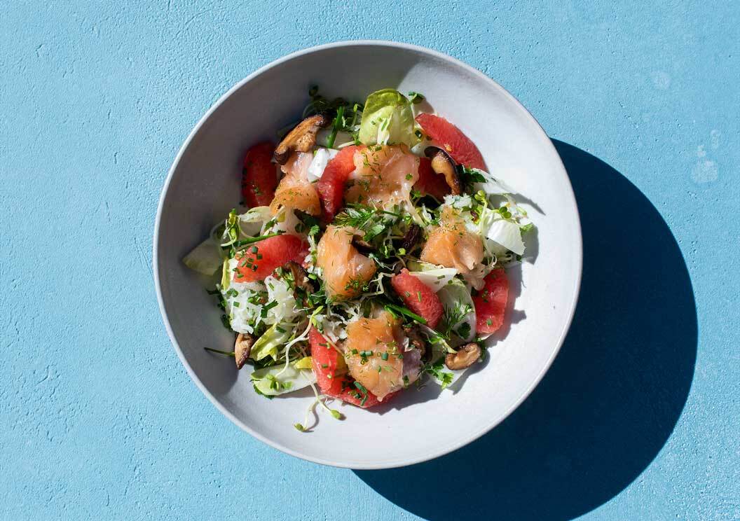 Frischer Kohlrabi-Sprossen-Salat mit Kräutern in einer weißen Schale auf blauem Untergrund.