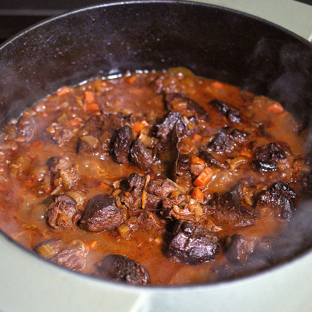Aroma­reicher Schmortopf mit dunklen Fleischstücken, Wurzelgemüse und kräftiger Sauce, langsam köchelnd in einem gusseisernen Topf – fotografiert für das Profil der Gewürzmühle Rosenheim.