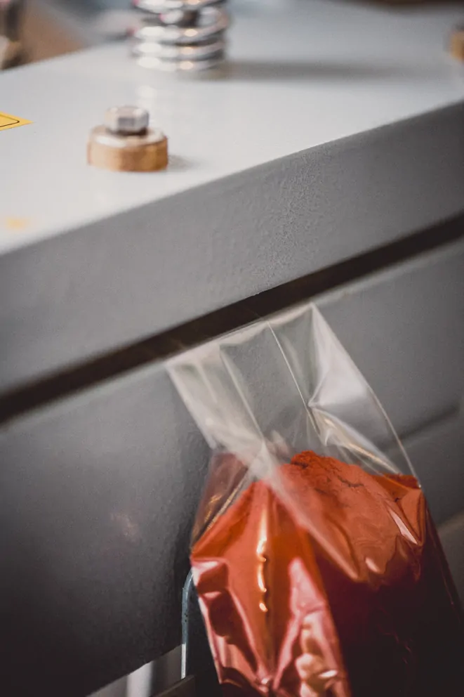 Metallpresse aus der eine Plastikverpackung mit einem roten Gewürz hervorragt