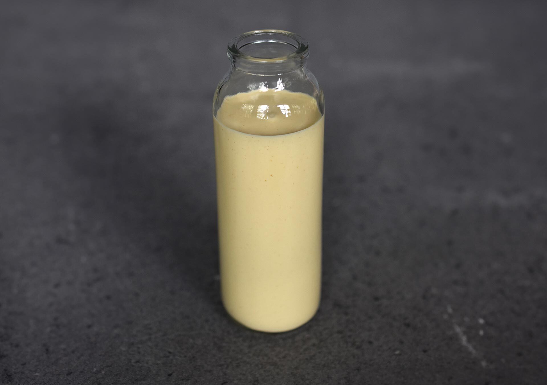 Glasflasche mit selbstgemachtem French-Dressing auf dunklem Untergrund