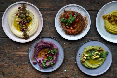 Fünf Teller mit Hummus-Gerichte, von oben fotografiert.