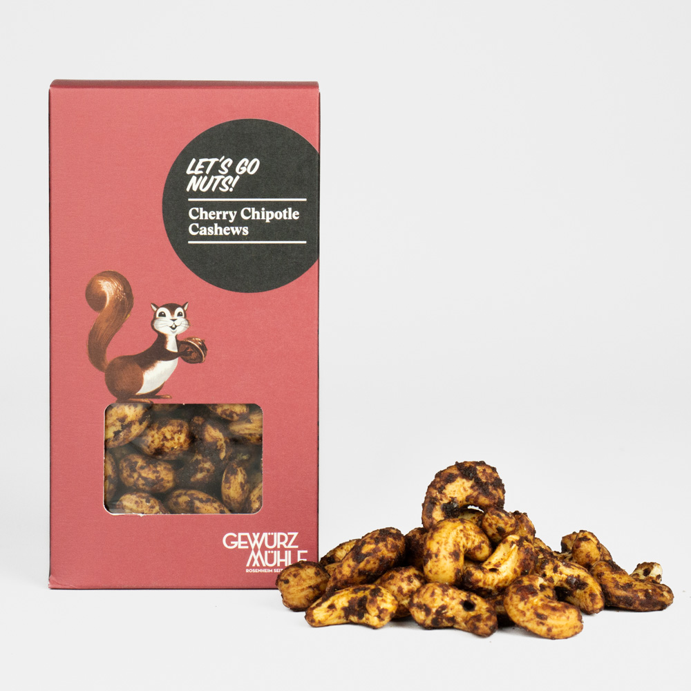 Nüsse in Pappverpackung mit Sichtfenster, ausgeschüttete Nüsse daneben - Cherry Chipotle Cashews
