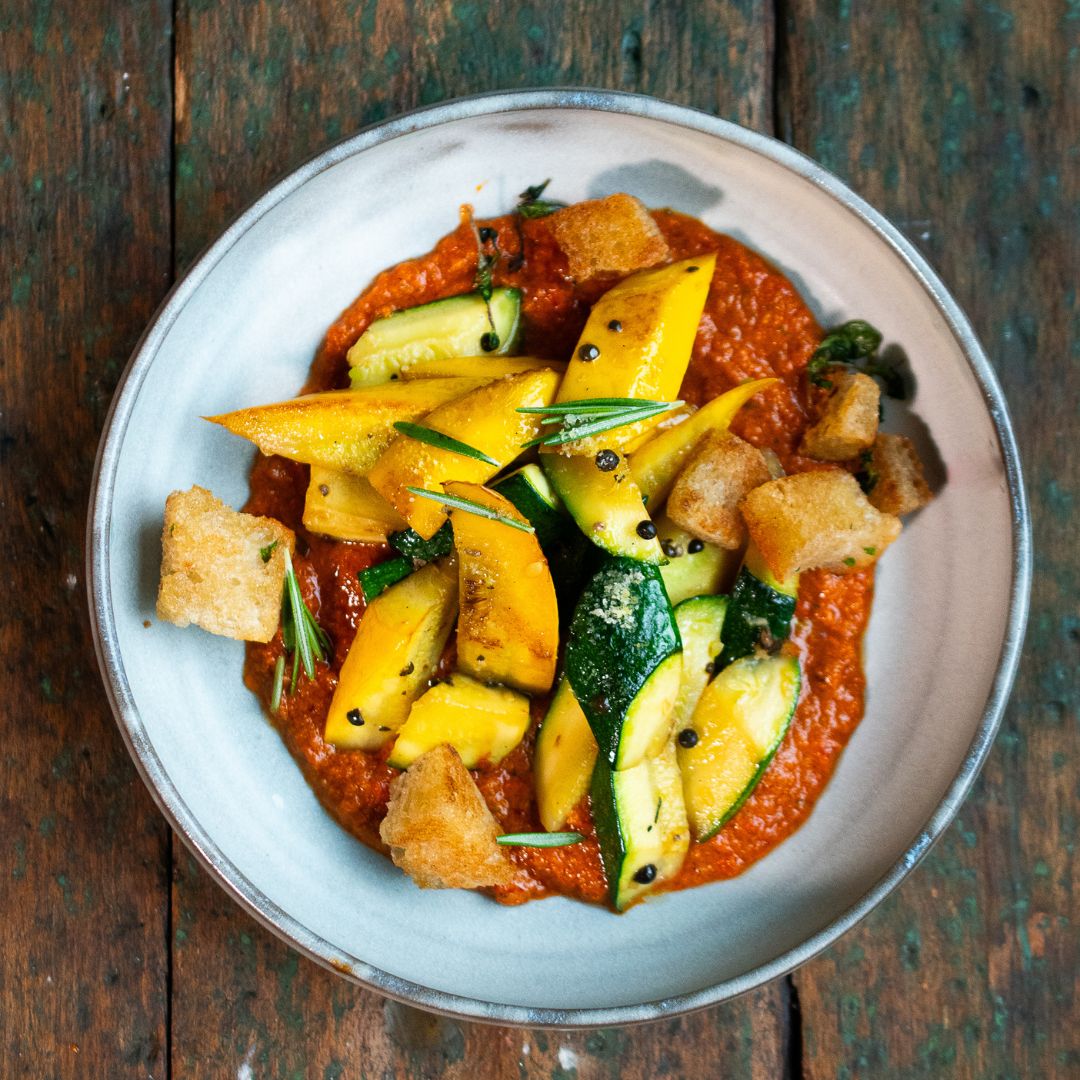 Gebratene gelbe und grüne Zucchinistücke auf würziger Tomatencreme, garniert mit knusprigen Brotwürfeln und Rosmarin. Serviert im Stil der Gewürzmühle Rosenheim.