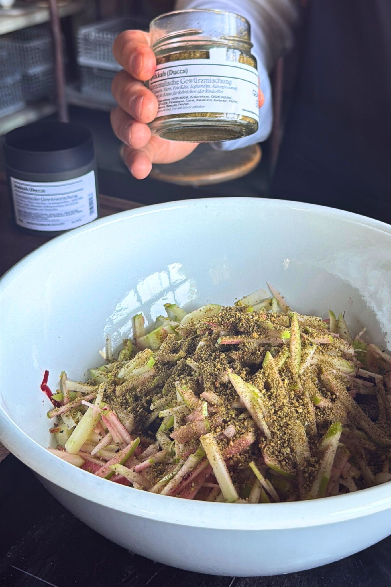Rote Bete und Apfelmischung mit Dukkah bestreut, während eine Hand das Dukkah-Gewürzglas hält