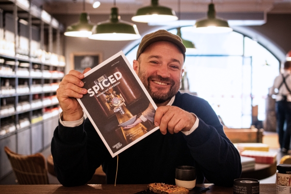 Simon Mendel an der Theke im Gewürzladen in Regensburg mit seinem Buch "SPICED - Kochen mit Gewürzen" in den Händen.