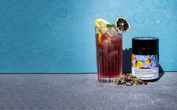 Eistee - Header mobile Mit Eistee gefülltes Glas neben einer Teedose, etwas Tee ist davor ausgeschüttet