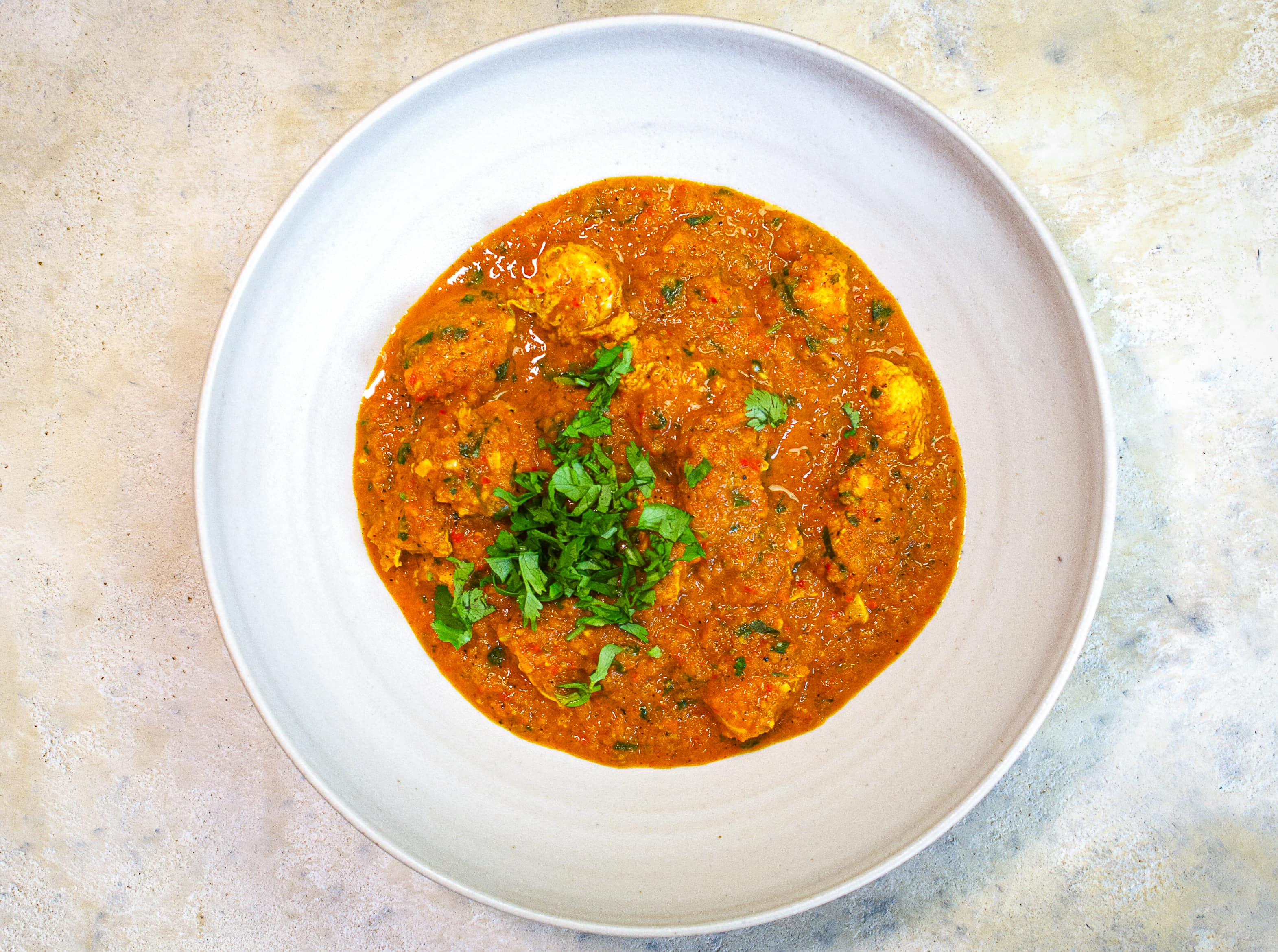 Ein Teller mit einer Portion Tikka Masala auf hellem marmorierten Untergrund.